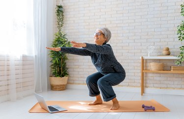 senior woman doing squats on an orange yoga mat at home
