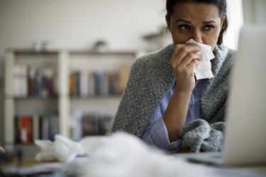 woman working at her desk and holding a tissue to stop her nosebleed