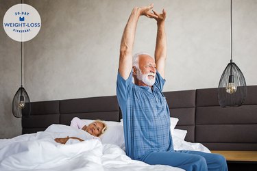 a person with white hair and beard in pajamas stretching before they get out of bed, to represent morning habits for weight loss