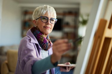 Person with blue glasses and short haircut painting on a canvas to help keep their brain sharp in their 50s.
